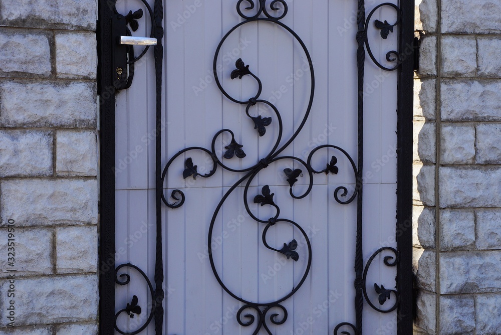 black wrought iron pattern on a gray metal door against a brick wall of a fence black wrought iron pattern on a gray metal door against a brick wall of a fence