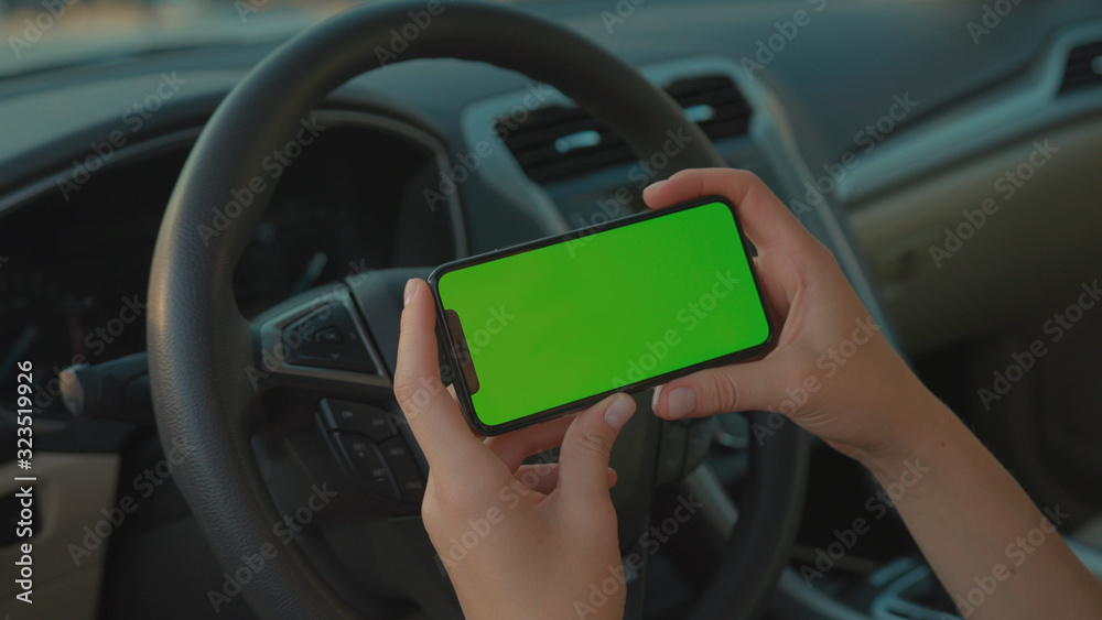 Lviv, Ukraine - May 19, 2018: Female driver sitting in the car browsing online map on vertical mock-up smartphone greenscreen searching route planning a roadtrip. Lifestyle and technology. Lviv, Ukraine - May 19, 2018: Female driver sitting in the car browsing online map on vertical mock-up smartphone greenscreen searching route planning a roadtrip. Lifestyle and technology.