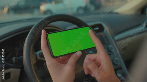 Lviv, Ukraine - May 19, 2018: Female driver sitting in the car browsing online map on vertical mock-up smartphone greenscreen searching route planning a roadtrip. Lifestyle and technology. © koshkin_stock