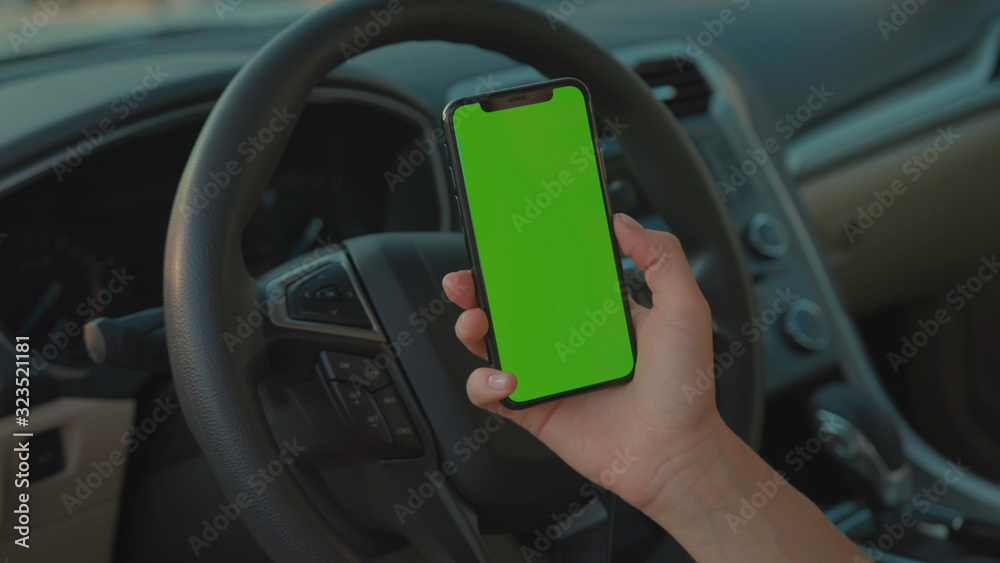 Lviv, Ukraine - May 19, 2018: Female driver sitting in the car browsing online map on vertical mock-up smartphone greenscreen searching route planning a roadtrip. Lifestyle and technology.