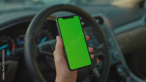 Lviv, Ukraine - May 19, 2018: Female driver sitting in the car browsing online map on vertical mock-up smartphone greenscreen searching route planning a roadtrip. Lifestyle and technology. © koshkin_stock