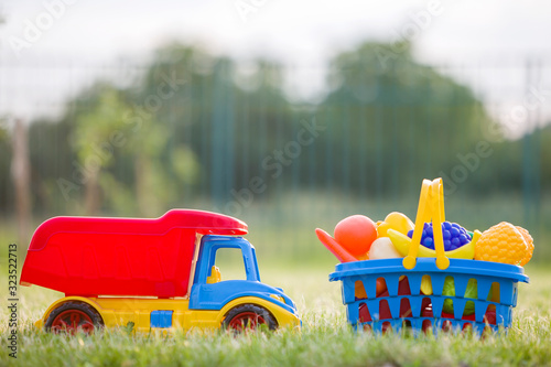 Car truckand a basket with toy fruit and vegetables. Bright plastic colorful toys for children outdoors on sunny summer day. photo