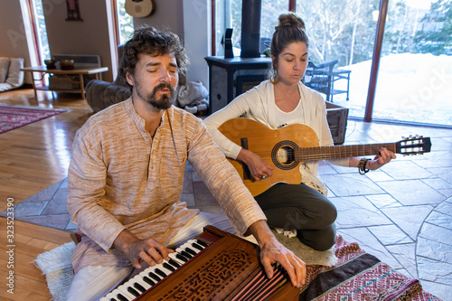 Young male and female meditators meditating while playing harmonium and classical guitar as sacred and kirtan music while sitting on floor in room
