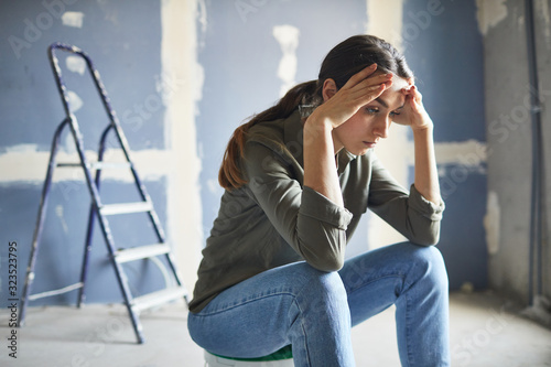 Portrait of frustrated young woman sitting on paint can devastated by renovations project, copy space