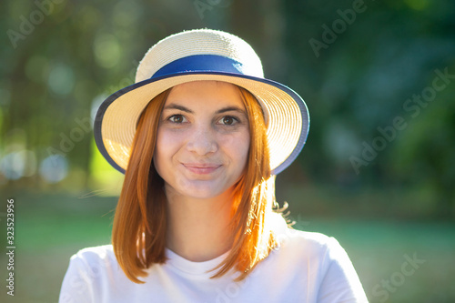 Closeup portrait of redhead hipster teenage girl in yellow hat smiling outdoors in sunny summer park. © bilanol