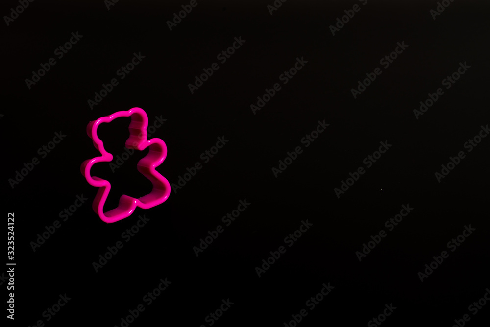 Pink plastic cookie cutter for making cookies in the shape of a teddy bear on a black background. Culinary concept. Flat lay with copyspace.
