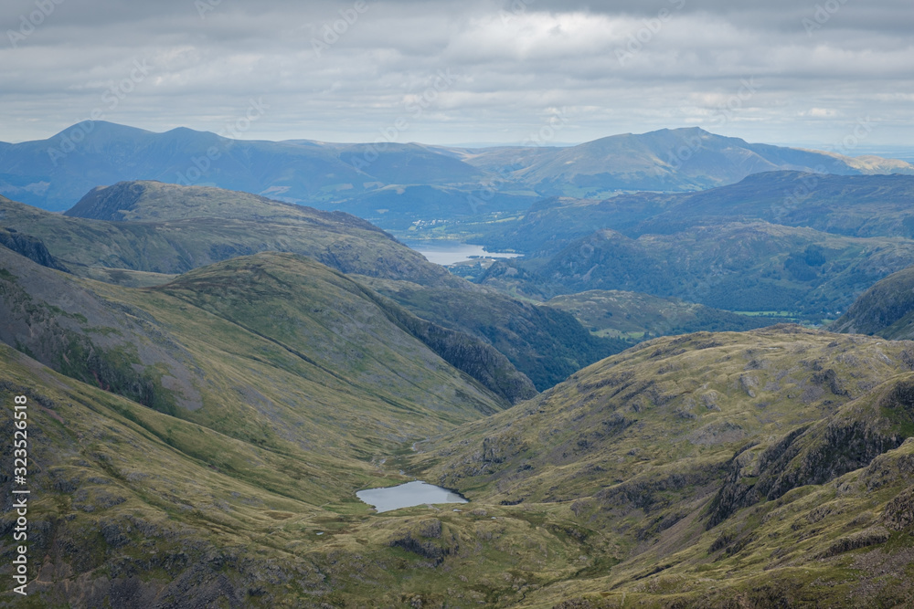 Green rolling hills from the summit of Scafell Pike towards Buttermere lake on an overcast and cloudy day