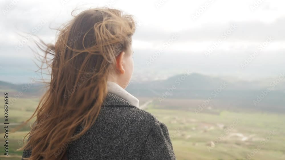 Wind flutters young girls hair. Young girl looking enjoying landscape, wind in her hair. Young girl hair is blowing in the wind