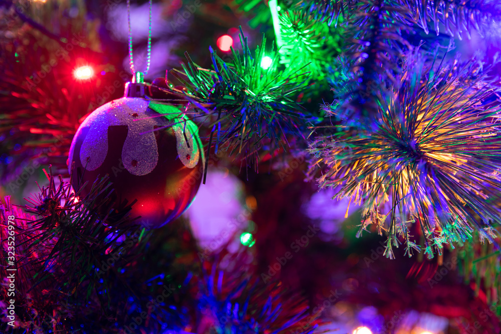 A close up photograph of a Christmas pudding bauble hanging from a green Christmas tree surrounded with multicoloured fairy lights
