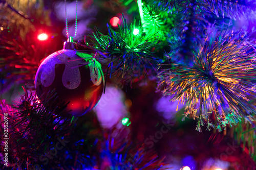 A close up photograph of a Christmas pudding bauble hanging from a green Christmas tree surrounded with multicoloured fairy lights
