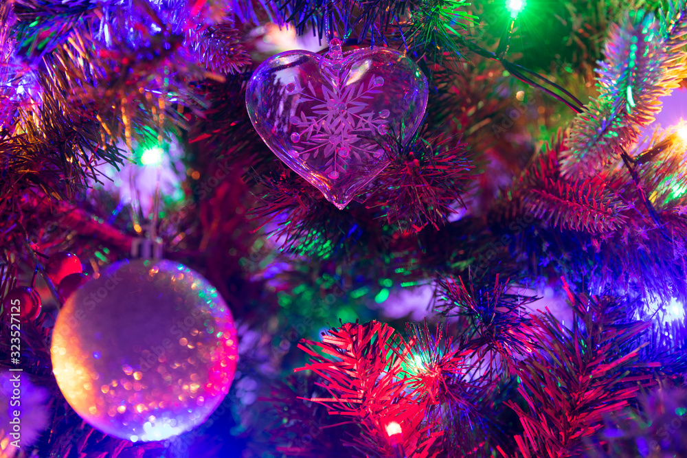 Multiple glass and glitter Christmas Baubles hanging from a green Christmas tree surrounded by fairy lights
