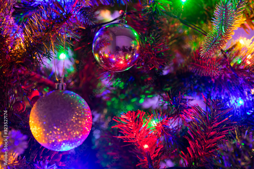 Multiple glass and glitter Christmas Baubles hanging from a green Christmas tree surrounded by fairy lights