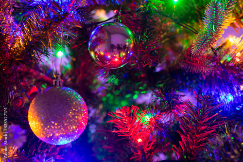 Multiple glass and glitter Christmas Baubles hanging from a green Christmas tree surrounded by fairy lights