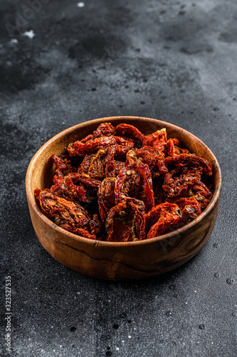 Sun dried tomatoes in wooden bowl. Black, dark background. Top view