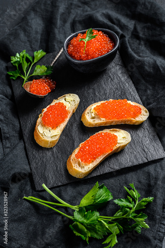 Red caviar in bowl and Sandwiches on stone board. Black background. Top view