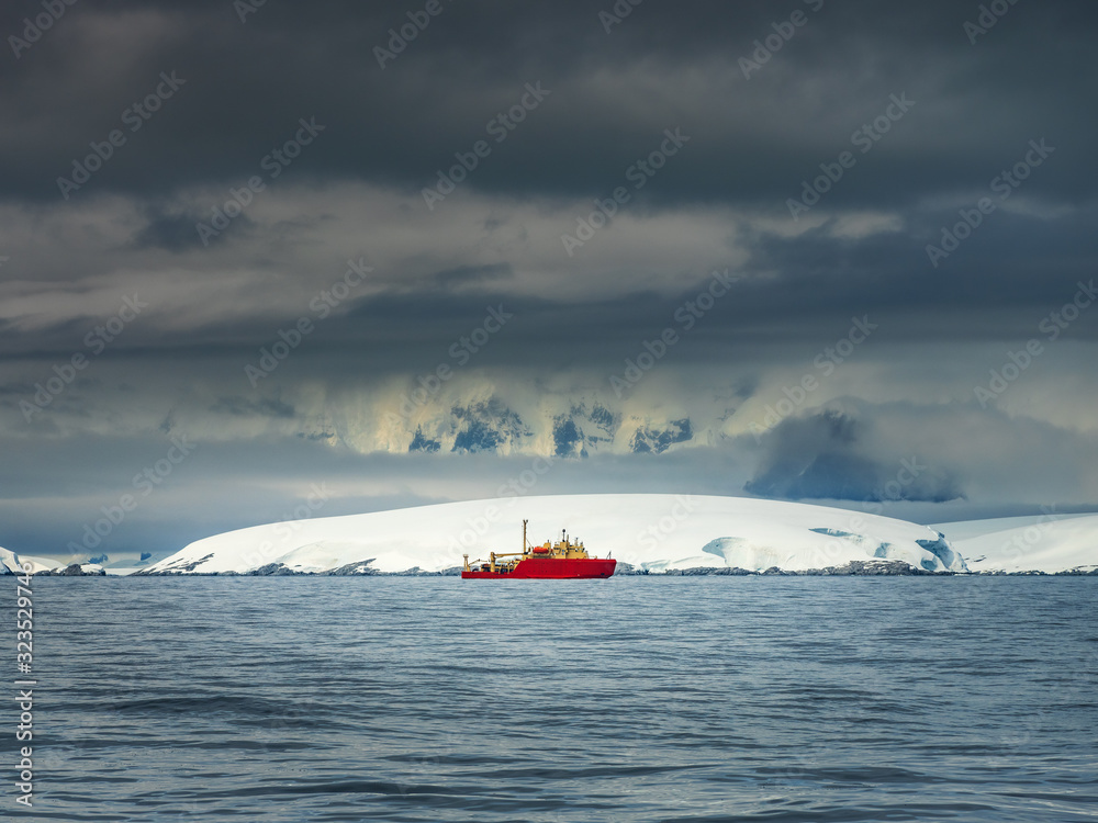 Fototapeta premium red research and science ship in Antarctic waters in day with dark clouds