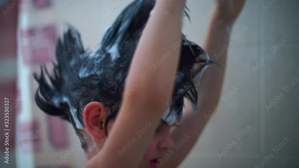 A cheerful boy in the bathroom makes a mohawk of his hair with soap