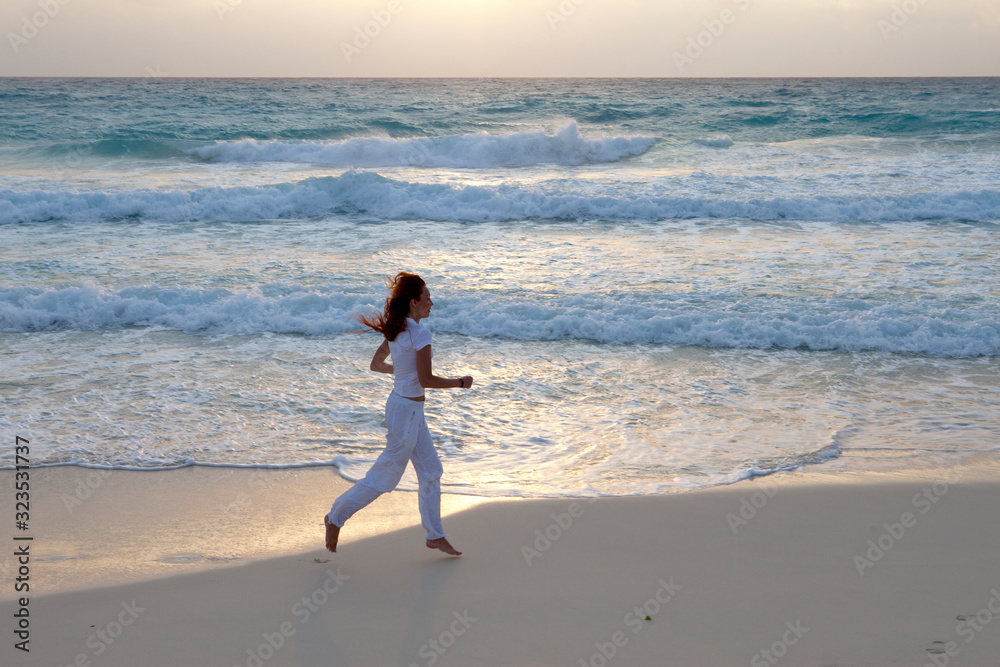 woman jogging on the edge of the sandy beach at sunrise