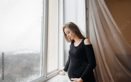 A pregnant girl is breathing fresh air from the window