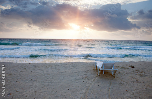 deck chair on the sandy beach of the sea with waves in the early morning sunrise..