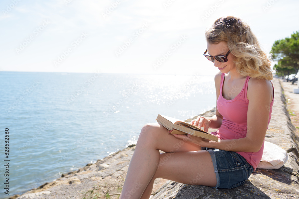 woman at the coast reading book in the sunshine