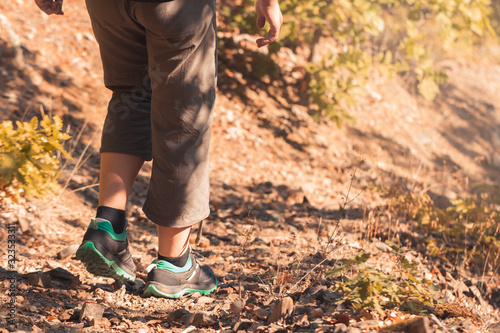 Hiking in mountains or forest with sport hiking shoes. Girl hiker walks along a wild path in a remote area. Active summer trekking adventure on a rocky road in a national park. Legs in boots in motion