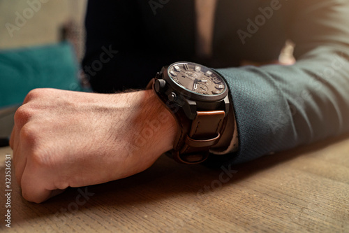 Closeup of black massive wrist watch with brown leather strap , man in elegant suit 