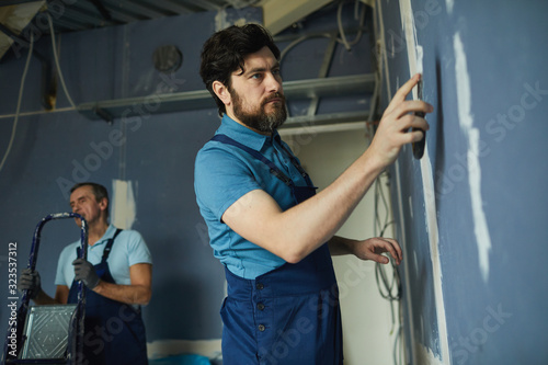 Side view portrait of bearded man working on dry wall while renovating house, copy space photo