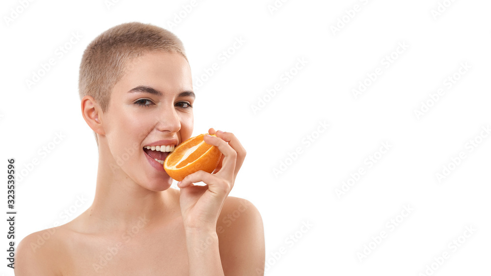 Food for healthy skin. Portrait of young and happy attractive blonde woman with short haircut eating a piece of orange and smiling at camera while standing against white background Food for healthy skin. Portrait of young and happy attractive blonde woman with short haircut eating a piece of orange and smiling at camera while standing against white background