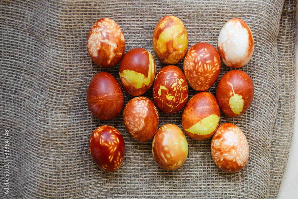 Obraz premium Chicken eggs colored with old-fashioned natural method by onion husks. Brown eggs with different natural patterns on beige burlap. Selective focus with copyspace. Traditional Easter and Spring concept
