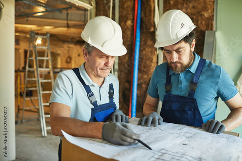 Waist up portrait of two construction workers wearing hardhats while looking at floor plans while renovating house, copy space photo