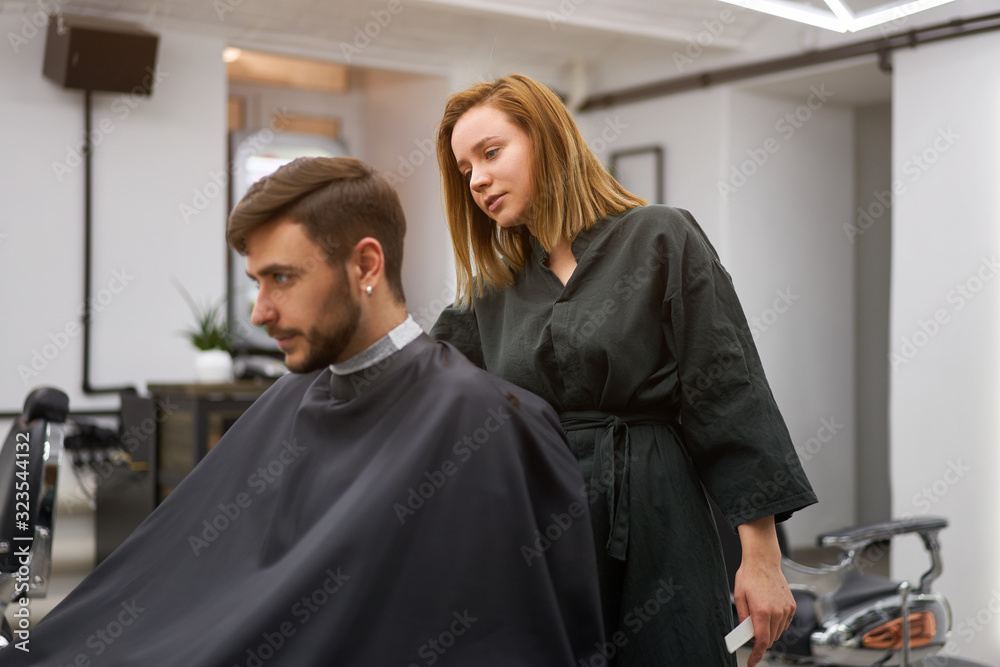 Handsome blue eyed man sitting in barber shop. Hairstylist Hairdresser Woman cutting his hair. Female barber. Handsome blue eyed man sitting in barber shop. Hairstylist Hairdresser Woman cutting his hair. Female barber.