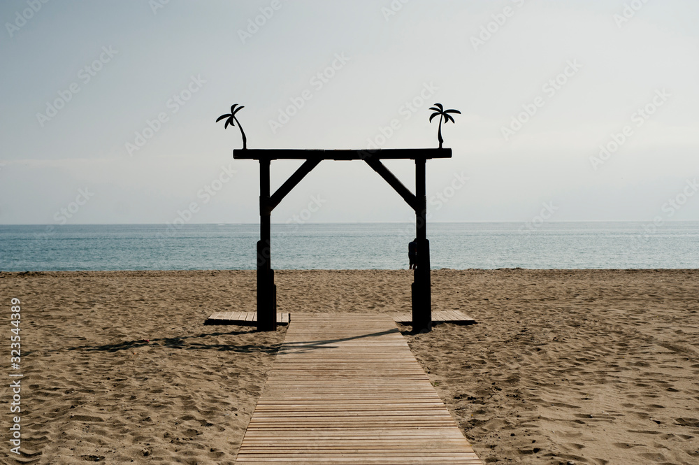beach landscape, with path and wooden arch, blue sky background sea, space to write