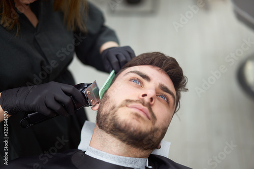 Young beautiful caucasian woman hairdresser cuts beard handsome man at modern barbershop
