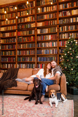 young beautiful couple sitting on the bed with two dogs on the background of the library and books in the apartment in the loft style © Alexander
