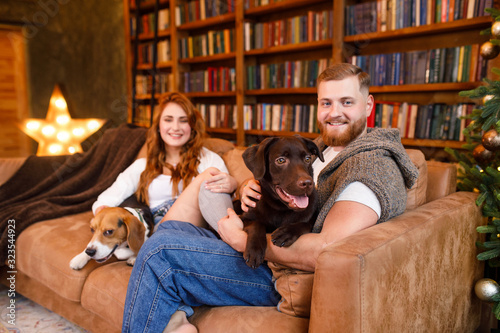 young beautiful couple sitting on the bed with two dogs on the background of the library and books in the apartment in the loft style © Alexander