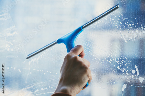young female hand cleaning dirty glass window with a squeegee photo