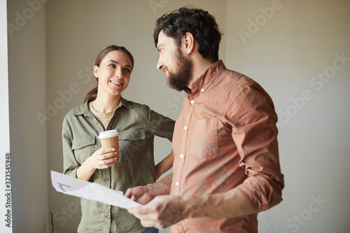 Waist up portrait of happy couple looking at color floor plans while redecorating house, copy space photo