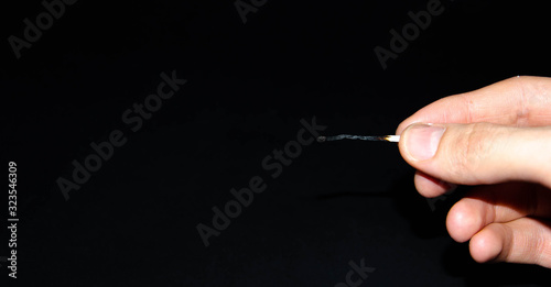 A hand holds a burning match on a black background. A wooden match burns in the hands of a macro. Igniting a match on a box. Smoke from a match. Flash