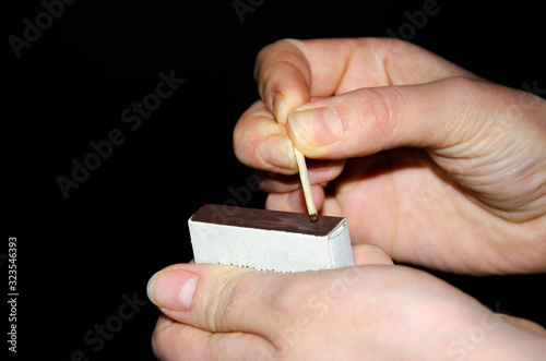 A hand holds a burning match on a black background. A wooden match burns in the hands of a macro. Igniting a match on a box. Smoke from a match.  Flash