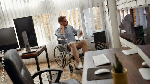 In search of inspiration. Portrait of young concentrated male office worker in a wheelchair looking at documents on white board in front of him in the bright modern office