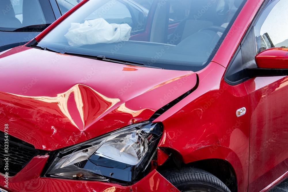 Red mini car severely damaged after traffic accident with deployed airbag