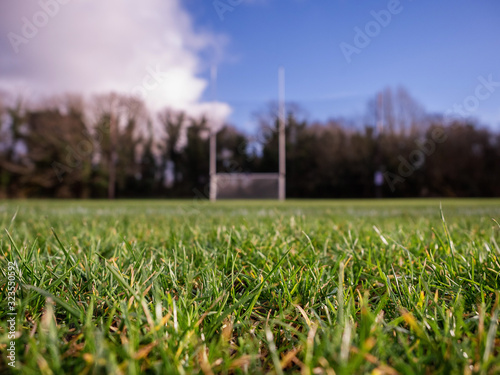 Grass on a pitch in focus, Irish national sport goalpost out of focus in the background. Concept football, rugby, hurling and camogie training.