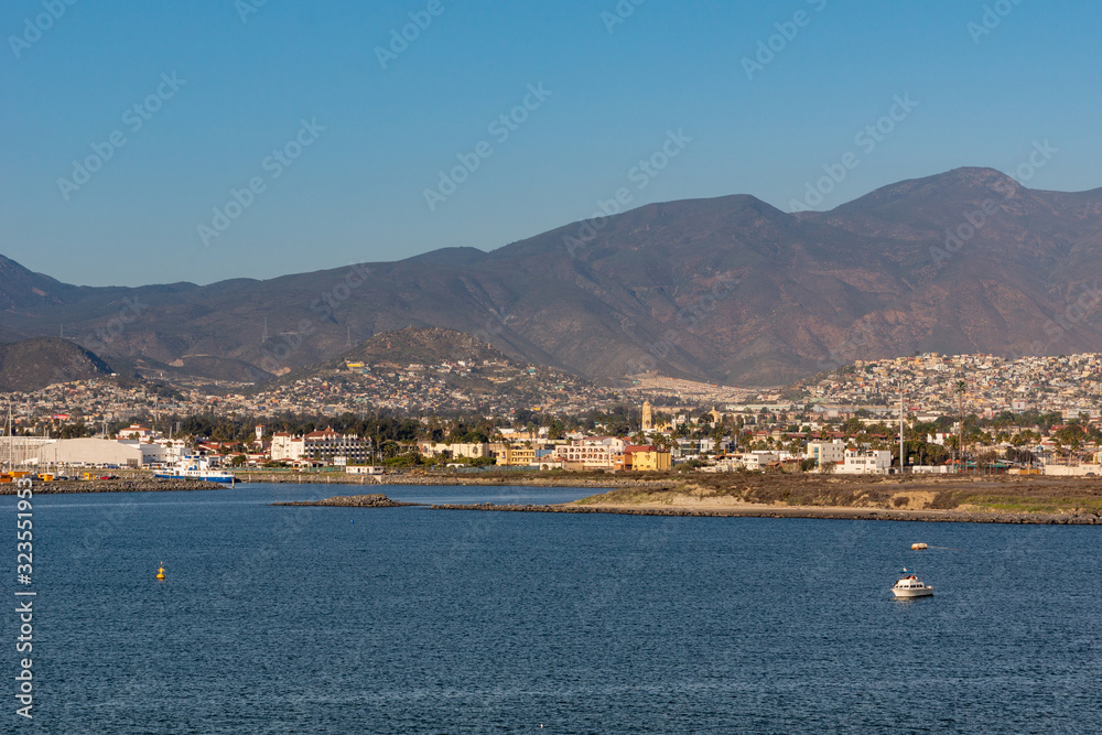 Ensenada, Mexico - January 17, 2012: Wide shot on cityscape with beige Cathedral tower on slopes of mountains under blue sky, from dark blue harbor waters.