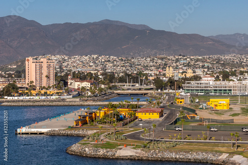 Ensenada, Mexico - January 17, 2012: Pink tall Villa Marina hotel and yellow Cathedral with its towers on other side behind port and in front of cityscape on slope of mountain under blue sky. photo