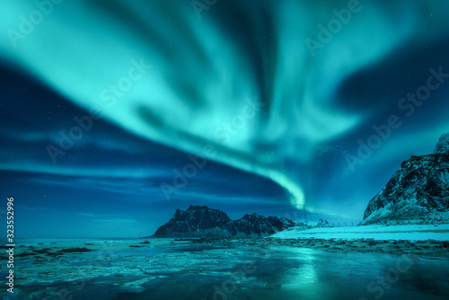 Fototapeta Aurora borealis over the snowy mountains and sandy beach in winter