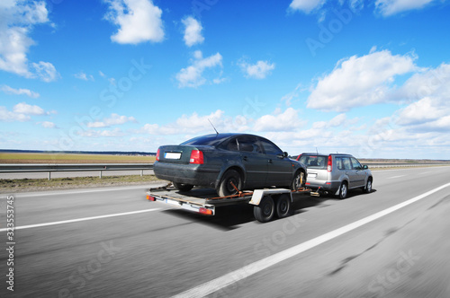 A crossover with trailer towing a car on the countryside road in motion against sky © Dmitry Perov