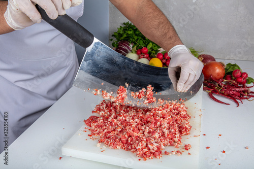 Chef is chopping the raw beef on cutting board with knife to cook in the kitchen, minced beef. Kebab restaurant, kebab preparation. photo