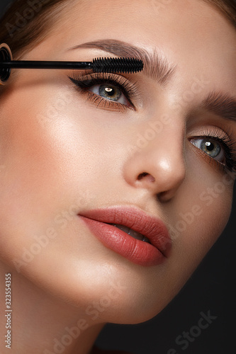 Beautiful girl with sexy lips and classic makeup with cosmetic mascara brush in hand. Beauty face. photo
