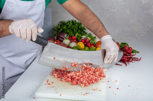 Chef is chopping the raw beef on cutting board with knife to cook in the kitchen, minced beef. Kebab restaurant, kebab preparation. photo